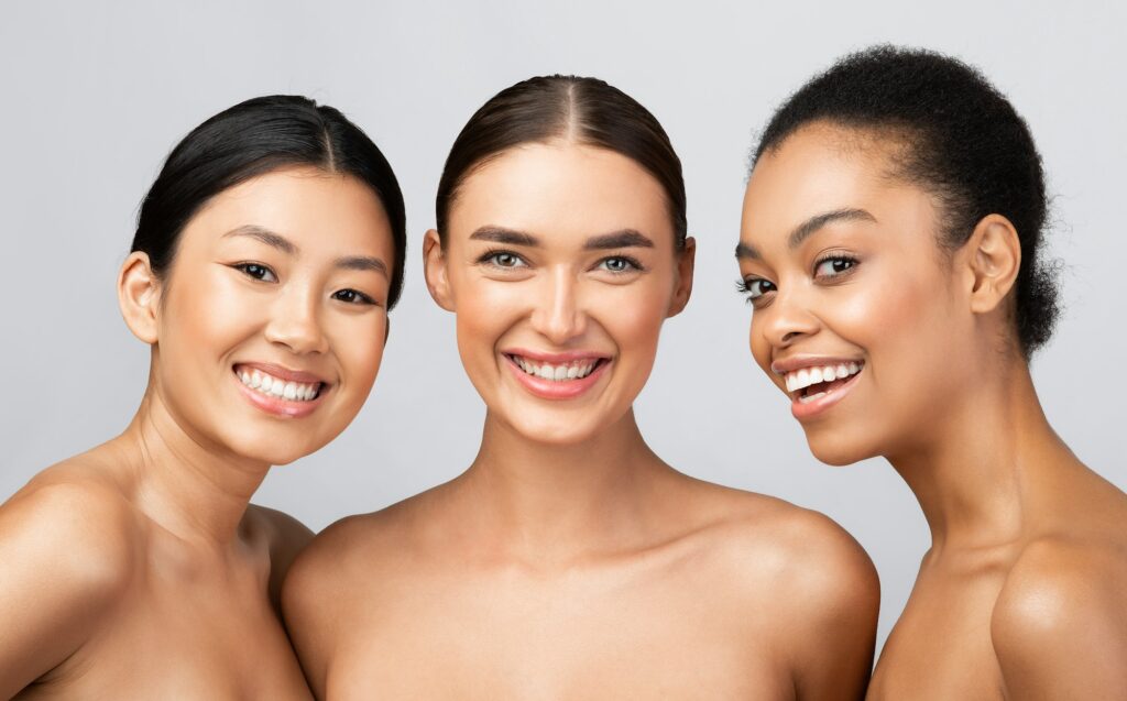 Three Diverse Models Women Smiling Posing Shirtless On Gray Background